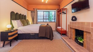 A bedroom with a bed, bedside table, lamp, window, and fireplace.