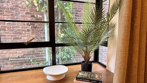A window with a brick wall, a potted plant, a white ceramic bowl, and books on a wooden ledge.