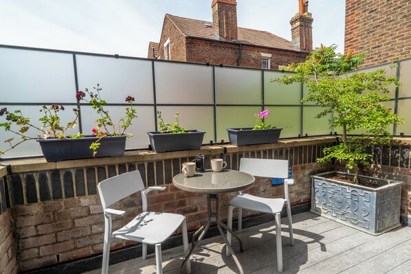 A patio with a round table and two chairs, potted plants, and a brick wall. - Art Deco studio with private terrace. Bright, comfortable base near Albert Road's restaurants and a short walk to the seafront. (Portsmouth)