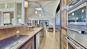 A modern kitchen with a central island, stainless steel appliances, and a view to the living area. - Sacred South Maui Beach House Sweeping Ocean Views Hot Tub Turtle Shore (Kihei)