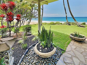 A patio with a view of the ocean, featuring a stone pathway, potted plants, and a small lawn area.