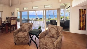 A spacious living area with a view of the ocean, featuring two patterned armchairs, a glass coffee table, and a dining table with chairs. - Sacred South Maui Beach House Sweeping Ocean Views Hot Tub Turtle Shore (Kihei)
