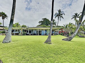 A modern house with a covered patio, surrounded by palm trees and a well-maintained lawn. - Sacred South Maui Beach House Sweeping Ocean Views Hot Tub Turtle Shore (Kihei)