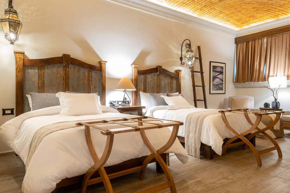 A bedroom with two wooden beds, a wooden nightstand, a ladder, and a wall-mounted lamp.