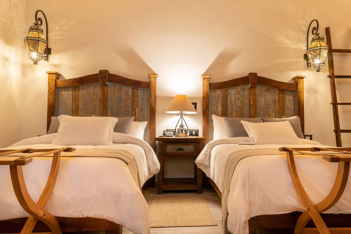 A room with two beds, a nightstand, and a lamp.
