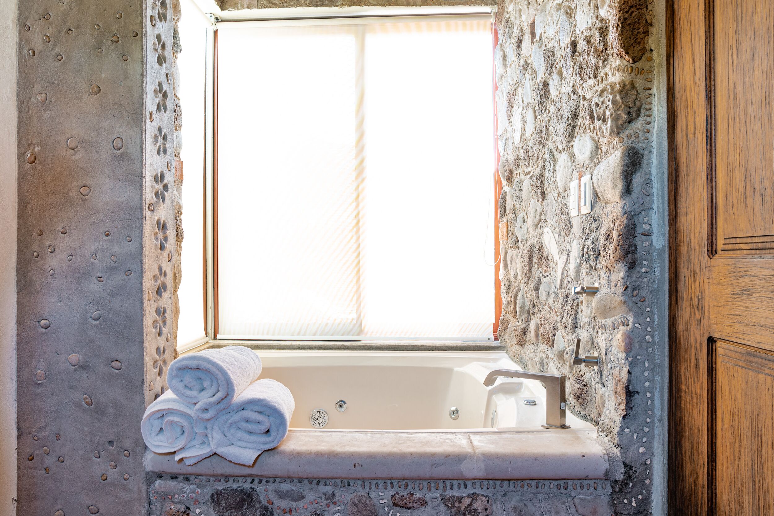 Une salle de bain avec un mur en pierre, une fenêtre, une baignoire et des serviettes enroulées.