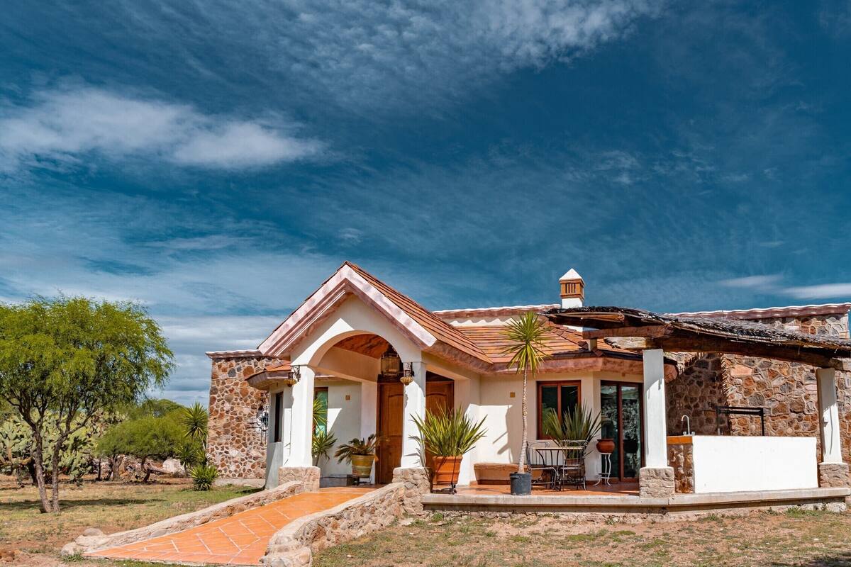 A house with a stone facade, a tiled roof, and a patio area with potted plants.
