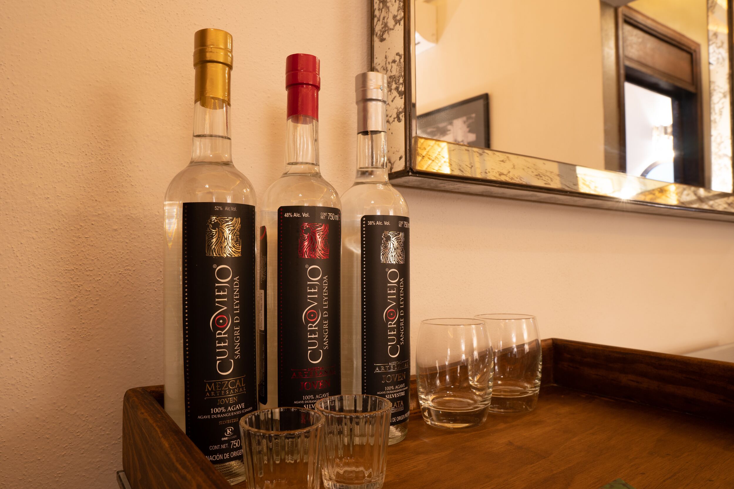 Tres botellas de licor Cueroviedo y cuatro vasos vacíos sobre una bandeja de madera.