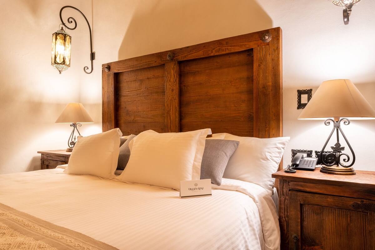 A neatly made bed with a wooden headboard, two bedside tables with lamps, and a small sign on the bed.