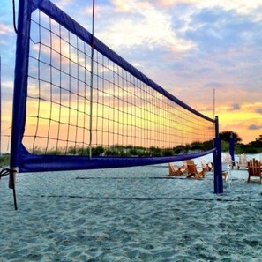 A beach volleyball net with chairs and a volleyball net on the sand.