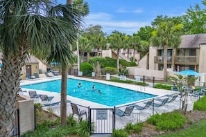 Una piscina circondata da palme e poltroncine da relax, con una recinzione e un cartello che indica il divieto di portare contenitori di vetro nell'area piscina.