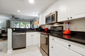 A modern kitchen with white cabinets, a black countertop, stainless steel appliances, and a red blender.