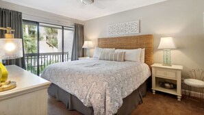 Un dormitorio con una cama grande, dos mesitas de noche, un ventilador de techo y vistas al exterior.