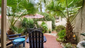 Un patio al aire libre con una mesa y sillas, rodeado de abundante follaje y una palmera.