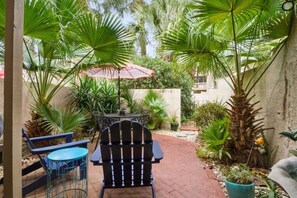 Patio esterno con tavolo e sedie, immerso nel verde e con una palma.