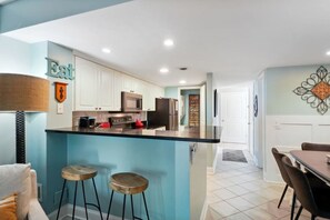 A modern kitchen with a central island, bar stools, and a dining area with a table and chairs. - Stylish Beach Retreat Walk to the Sand from Beach (Hilton Head Island)