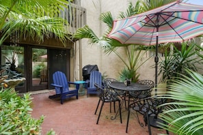 An outdoor patio with blue chairs, a round table, and a striped umbrella.