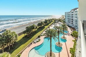 A resort with a pool area, palm trees, and a view of the beach and ocean.