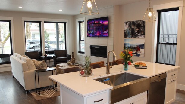 A modern kitchen with a central island, stainless steel appliances, and a dining area with a sofa and chairs. - Stunning Downtown Home on Sherman Avenue (Coeur d'Alene)