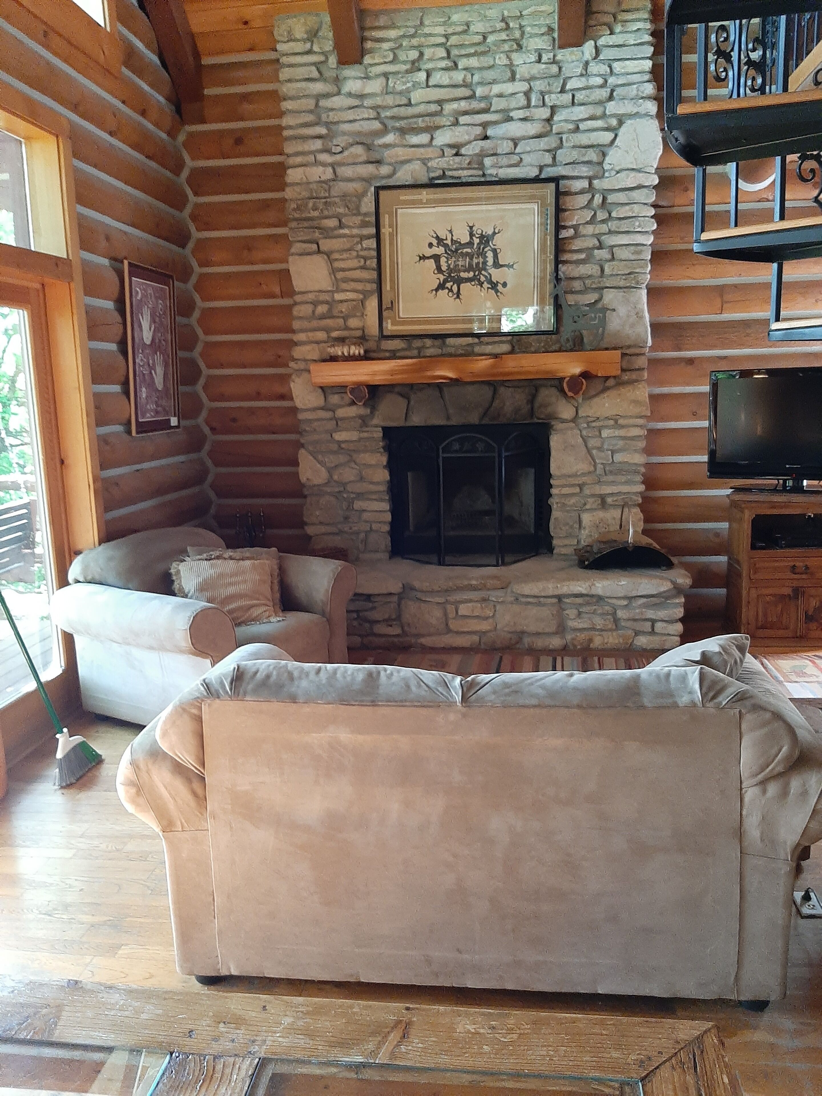 L’intérieur d’un chalet confortable, avec des murs en rondins de bois, une cheminée en pierre, un canapé et un téléviseur.
