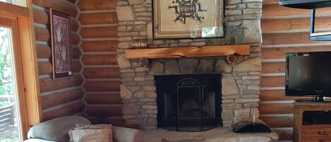 Interior acogedor de una cabaña de madera con chimenea de piedra, un sofá y un televisor.