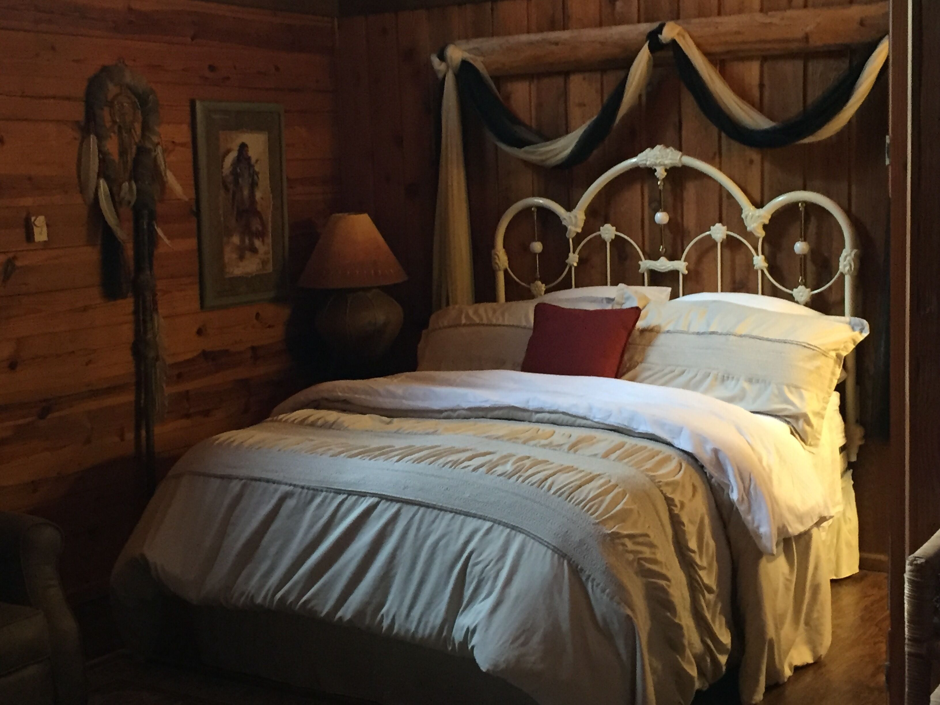 A wooden cabin-style room with a bed, a lamp, and a wall-mounted picture.