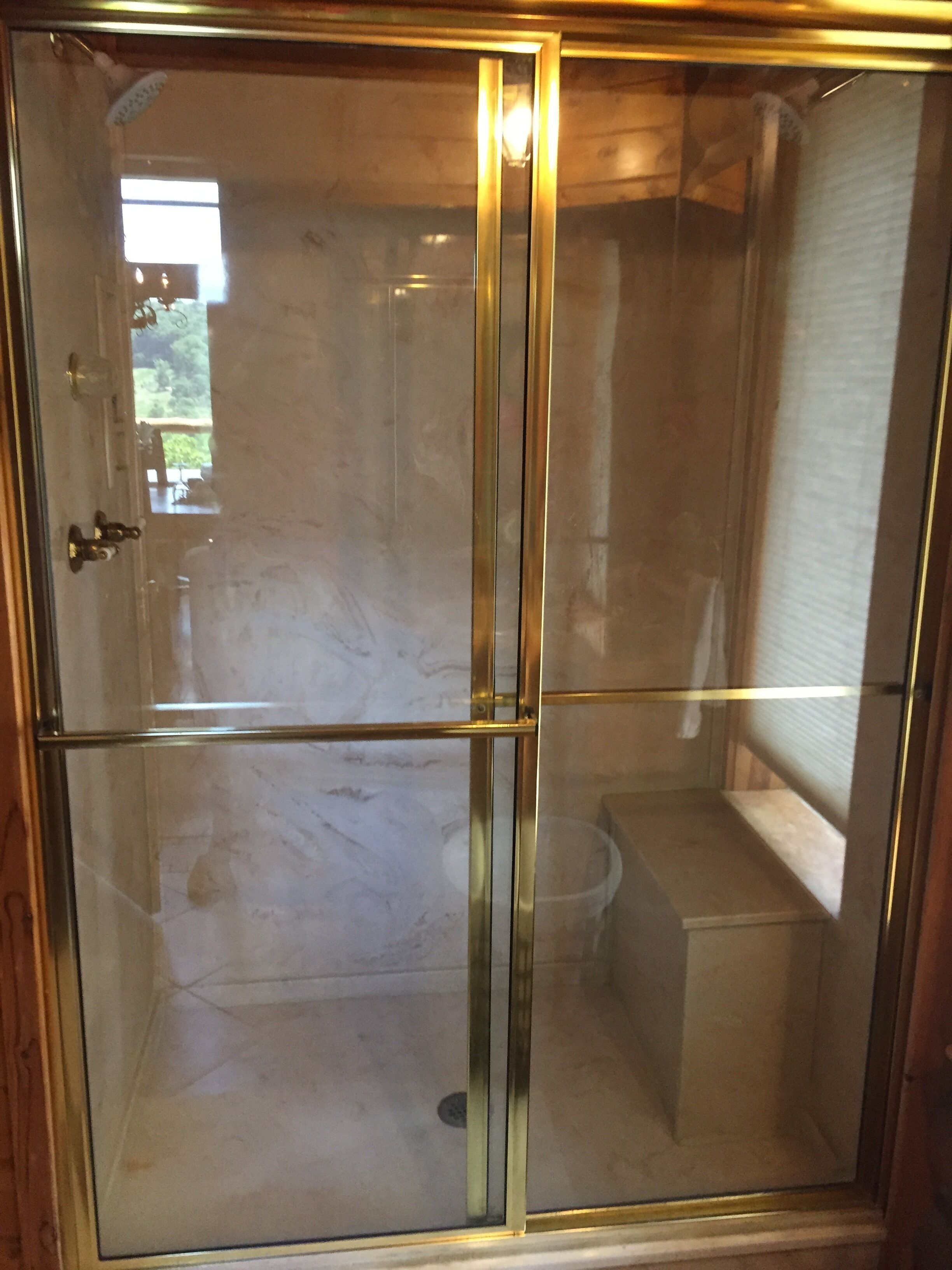 Un espace douche clos par des parois de verre, avec une structure en bois et des toilettes visibles.