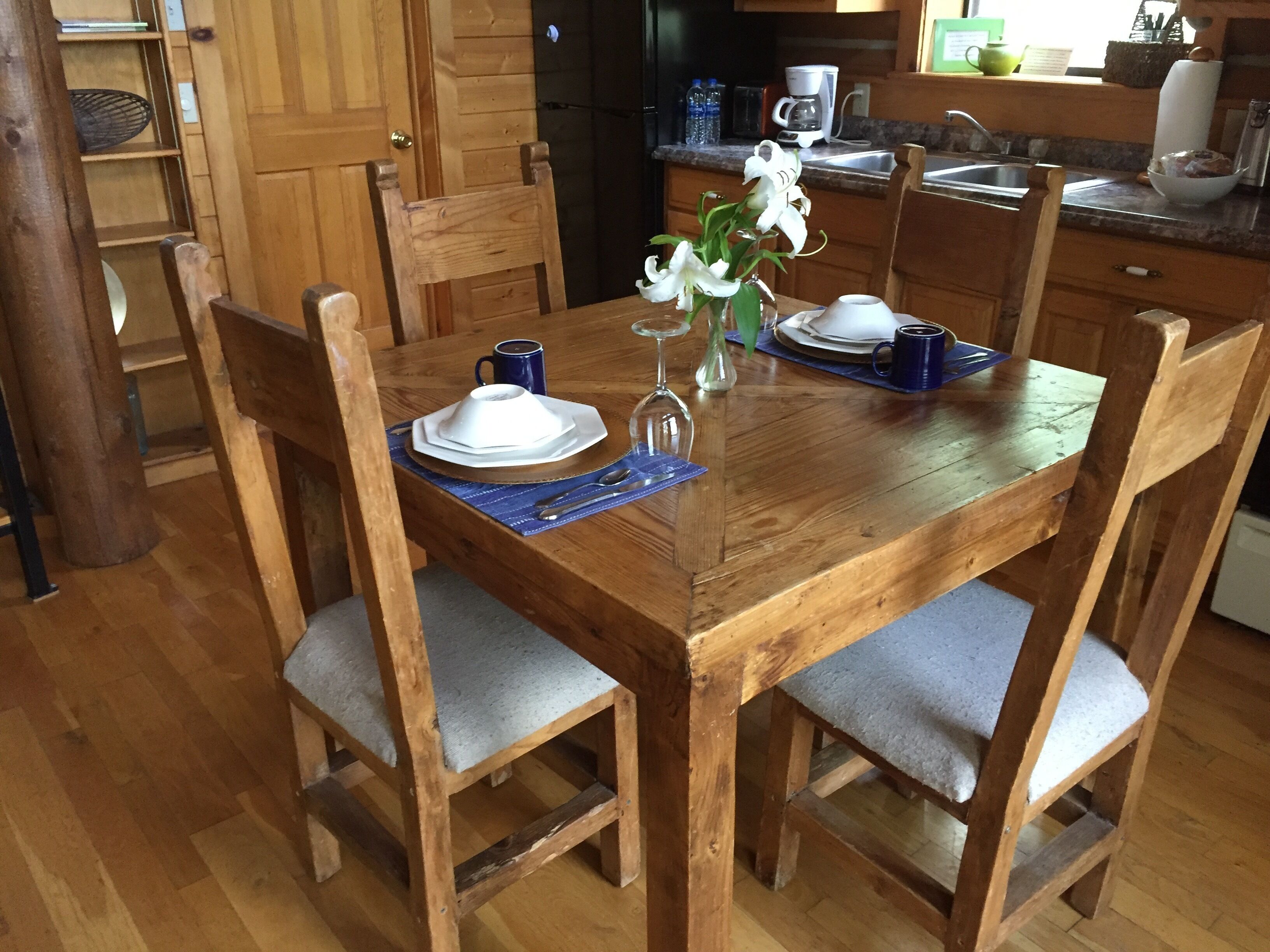 A wooden dining table with chairs, a vase with flowers, and a coffee maker in a kitchen.