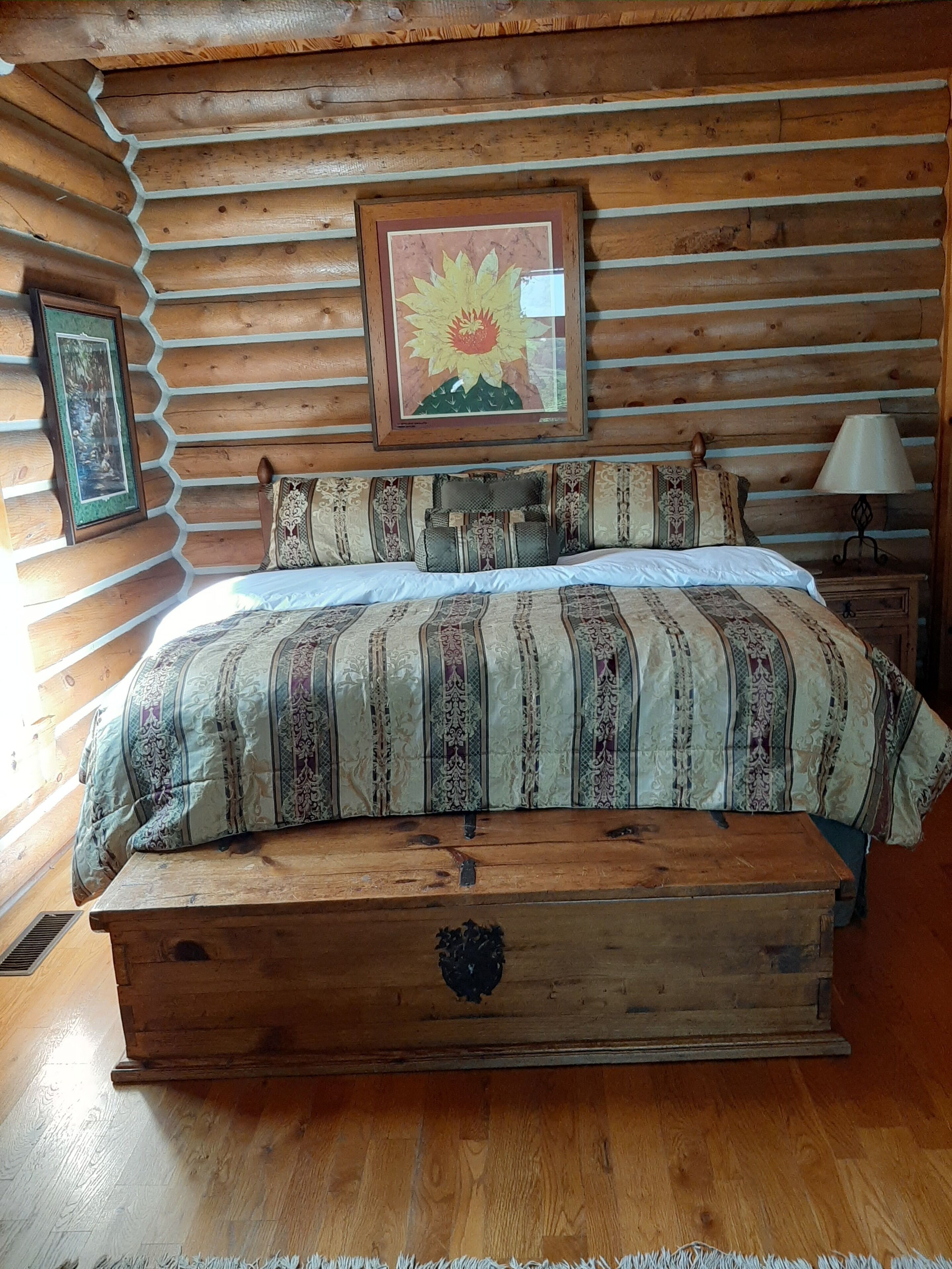 Un dormitorio tipo cabaña de madera con una cama, cuadros enmarcados y una mesita de noche de madera.