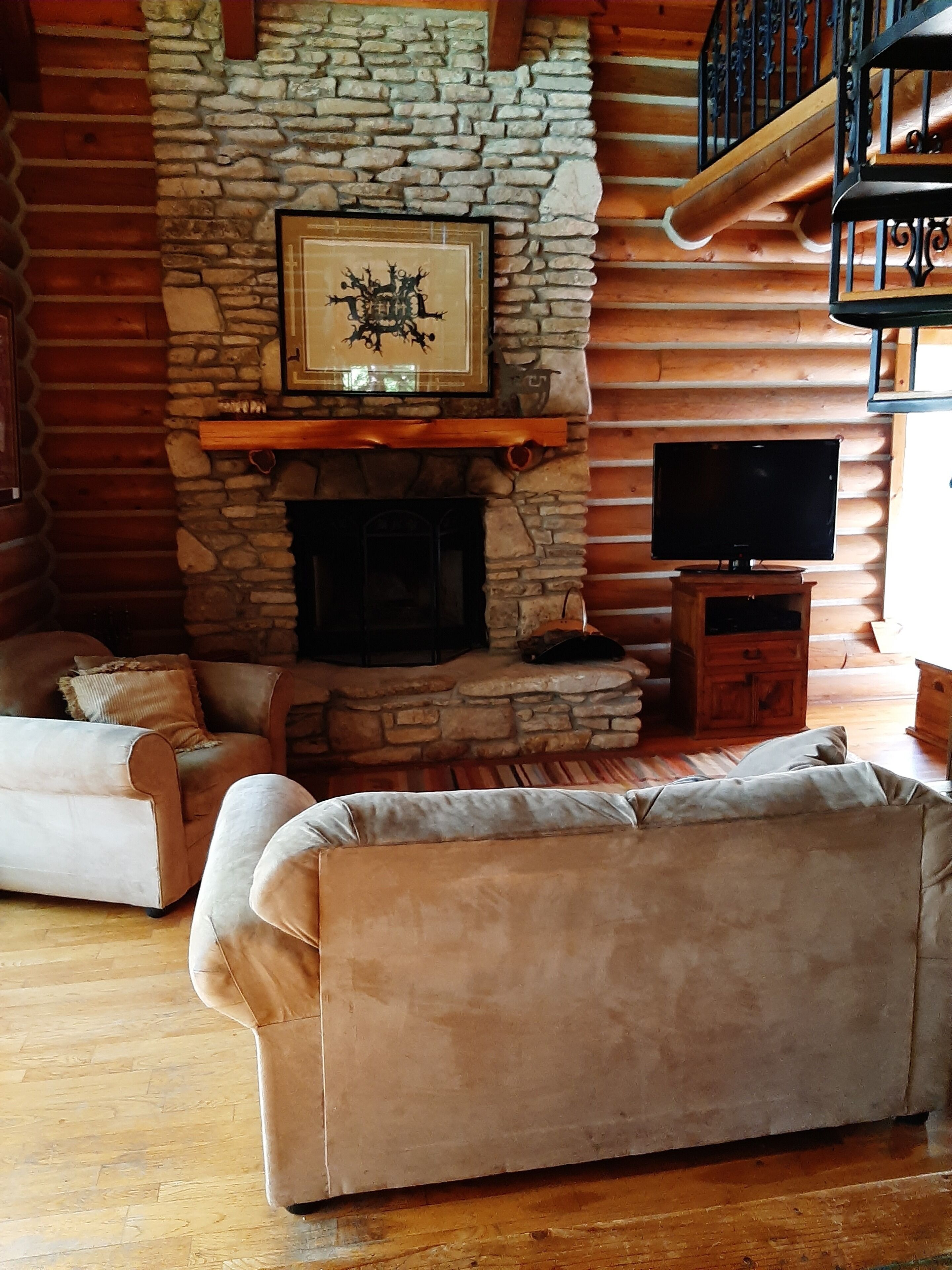 A cozy living room with a stone fireplace, a mounted television, and two sofas.