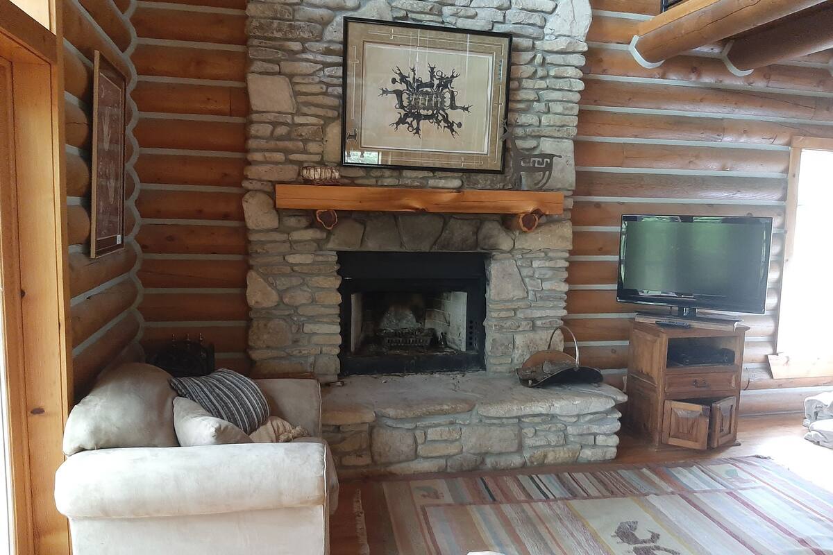 A cozy log cabin interior with a stone fireplace, a television on a wooden stand, and a plush sofa.