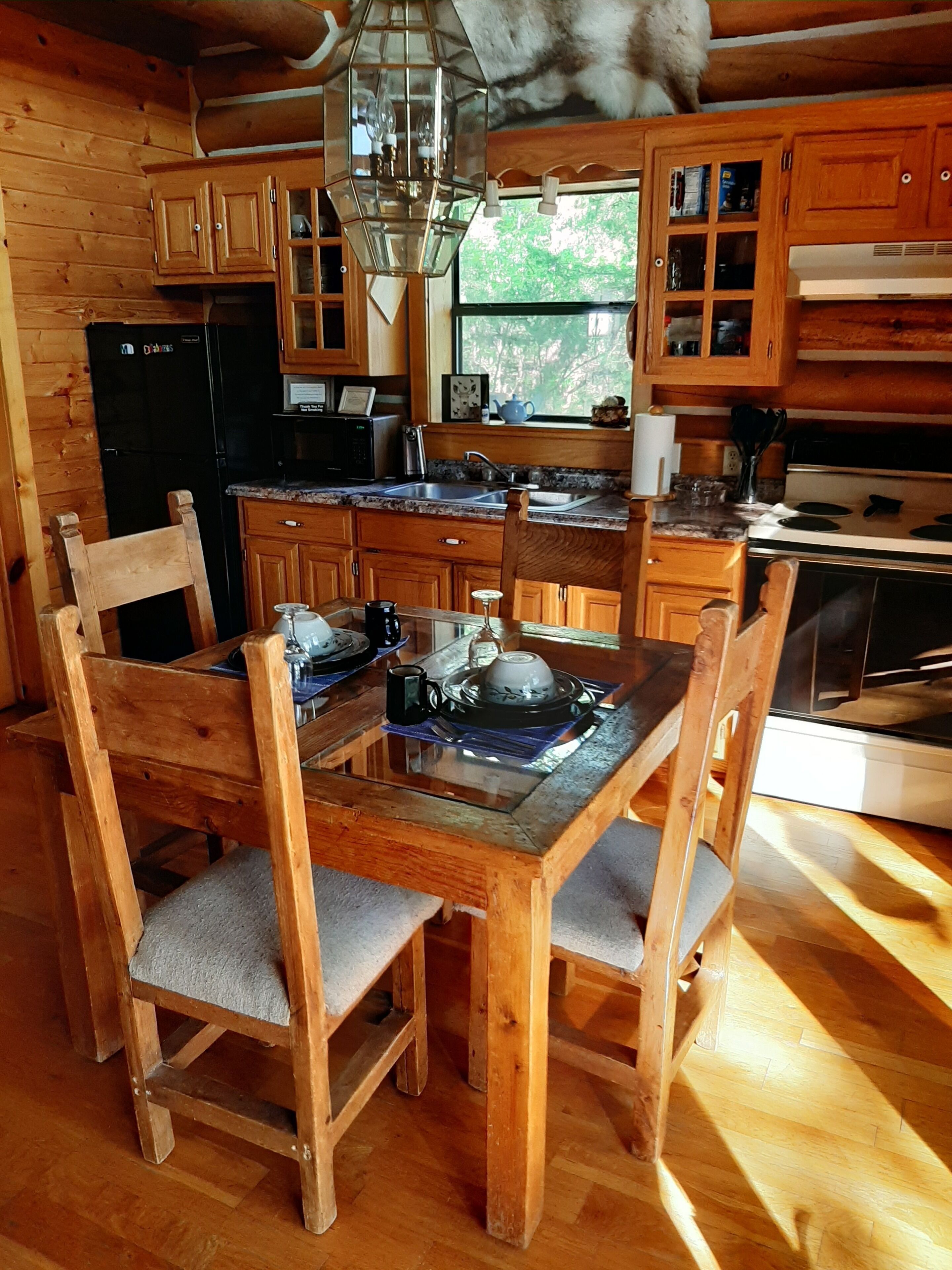 Een rustieke houten keuken met een eettafel en stoelen, een koelkast, fornuis en kastjes.