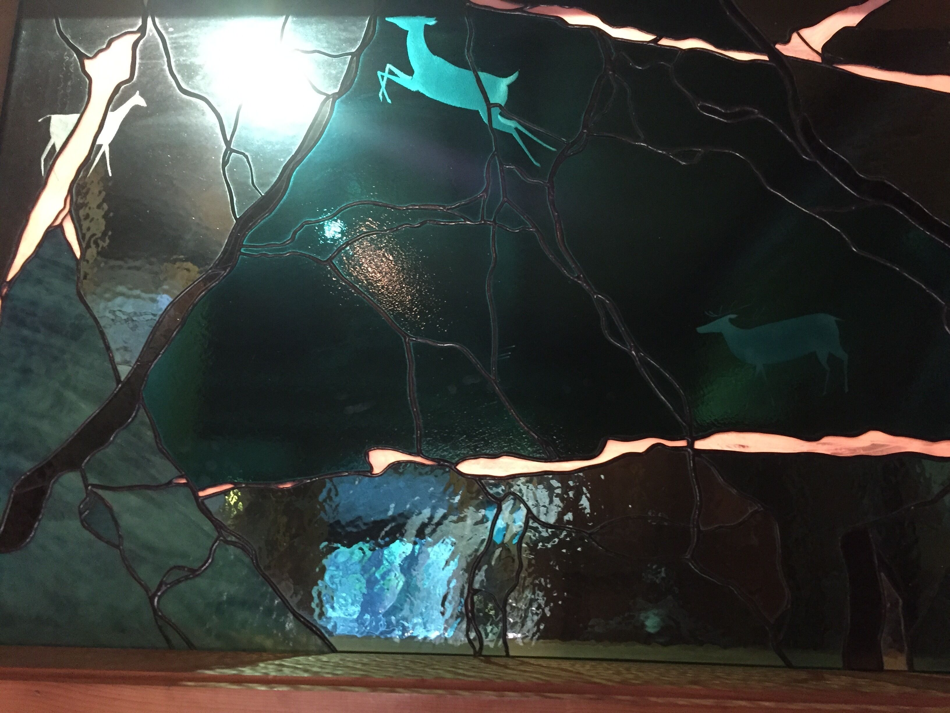 A stained glass window with deer silhouettes and a forest scene.