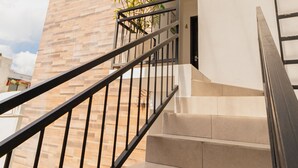 Eine Treppe mit Handlauf führt zu einer Tür, umgeben von einem modernen Gebäude mit Glasdach und Pflanze.
