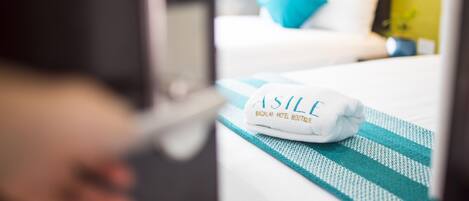 Habitación de hotel con una cama bien tendida, una almohada azul y una toalla con el texto "ASILE".