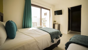 Ein Schlafzimmer mit einem Bett, einem an der Wand befestigten Fernseher und einem Fenster mit Vorhängen.