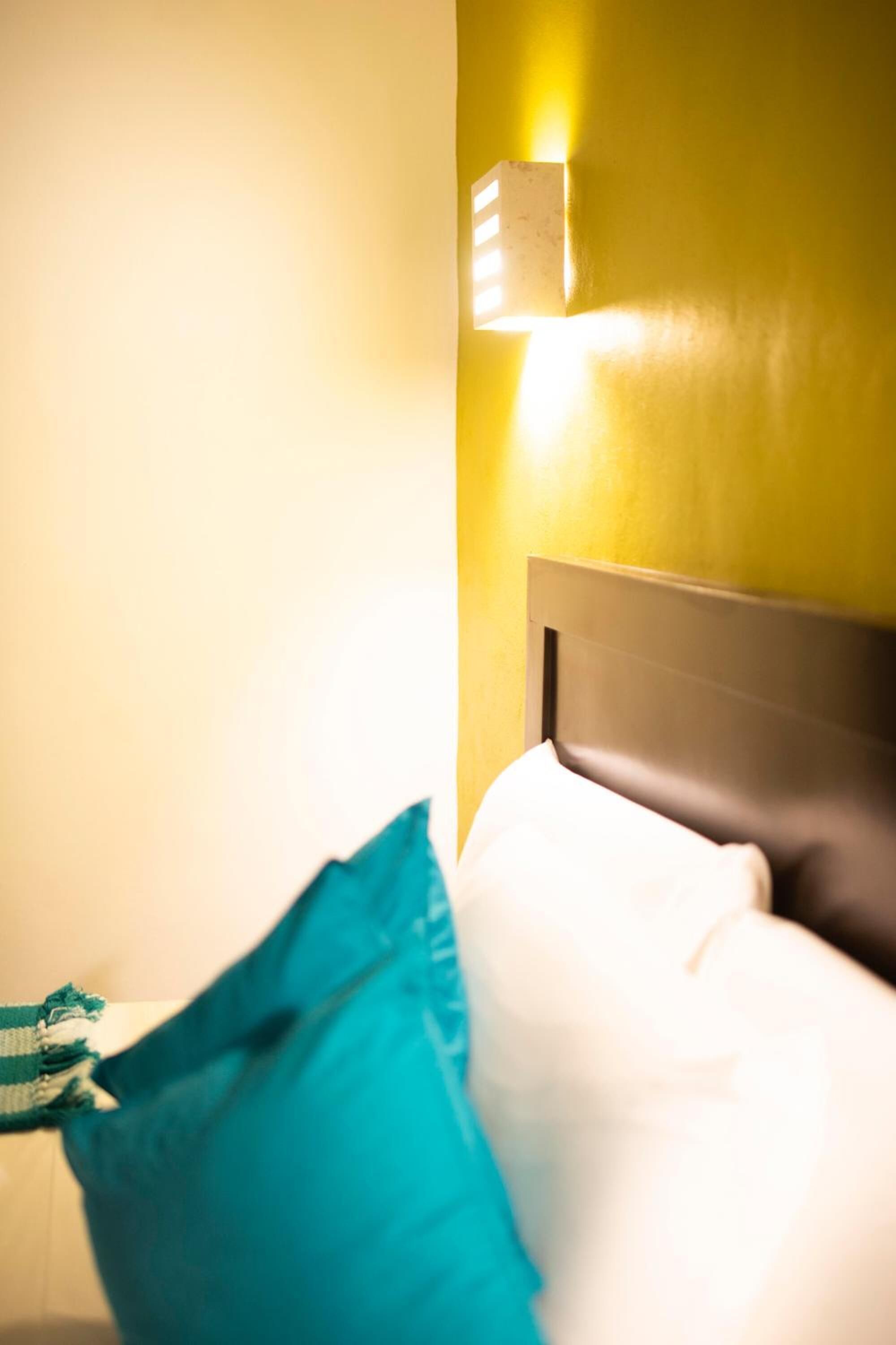 Una habitación de hotel con una cama, una mesita de noche y una lámpara de pared.