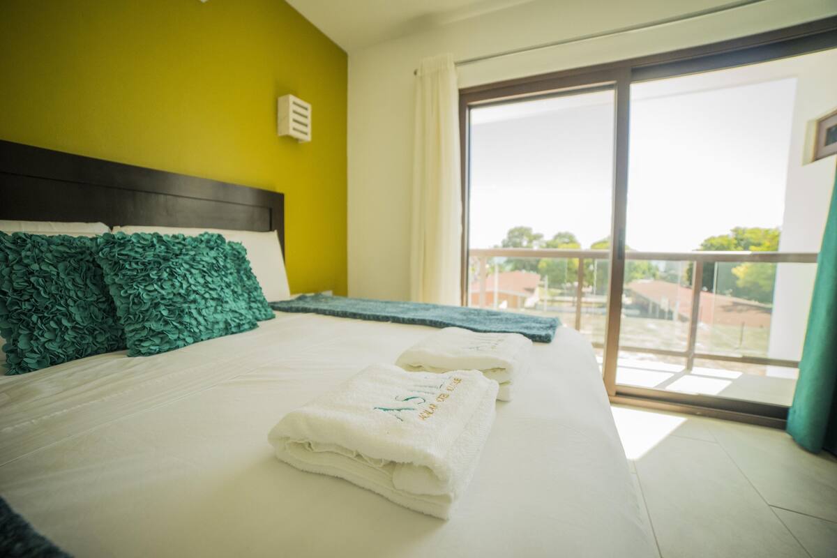 Una habitación de hotel con una cama, un ventanal con vistas y una pared verde.