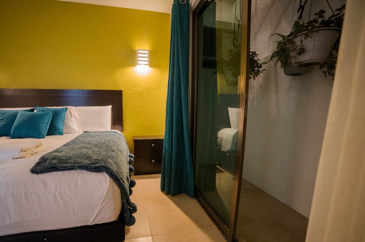 A hotel room with a bed, a nightstand, a wall-mounted light, a sliding glass door, and a hanging plant.