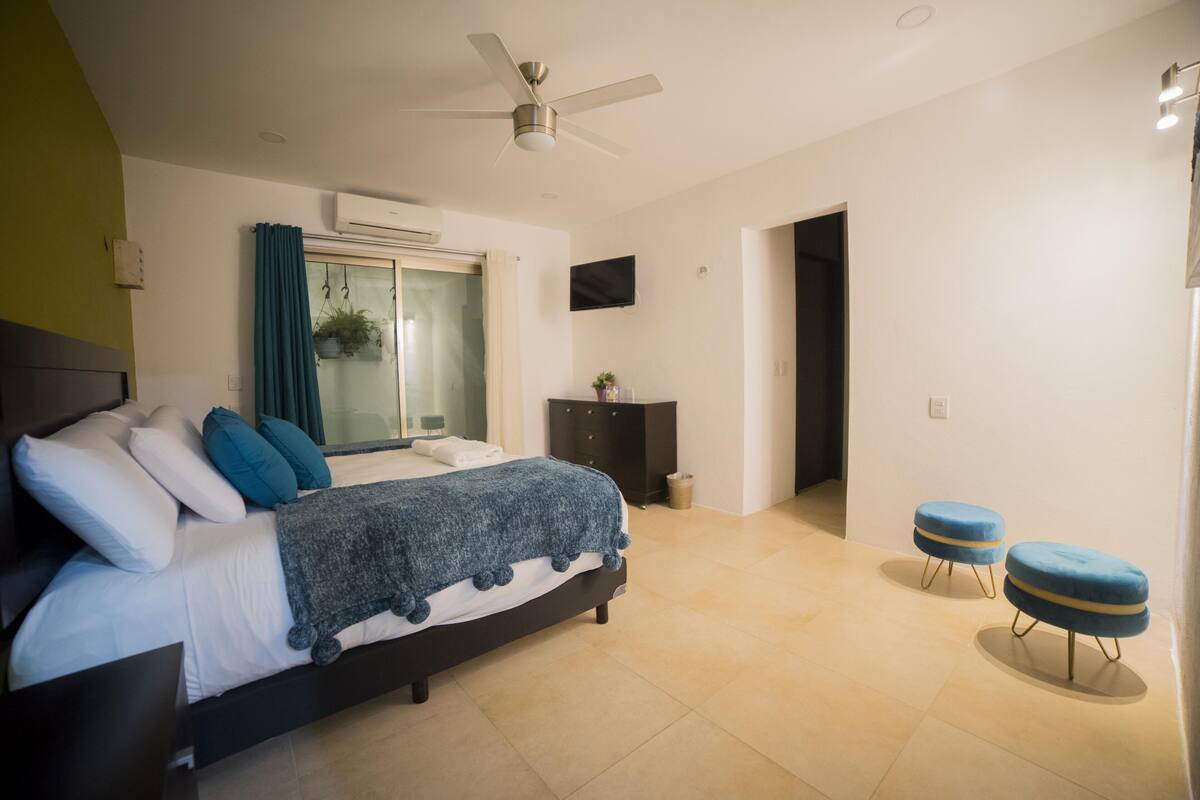 Un dormitorio con cama, ventilador de techo, televisor y ventana con cortinas.