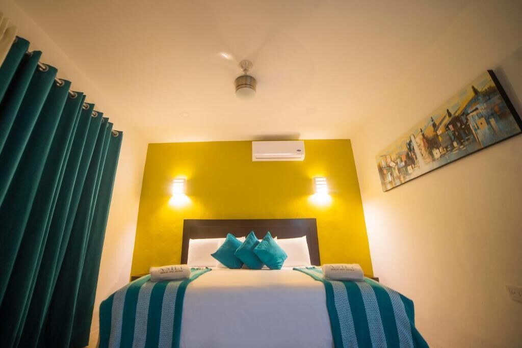 A hotel room with a bed, curtains, an air conditioning unit, and a painting on the wall.