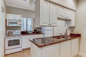 Una cocina con gabinetes blancos, encimera de granito, estufa y pileta.