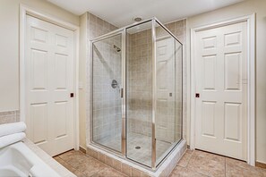 A bathroom with a glass-enclosed shower, white doors, and a bathtub.