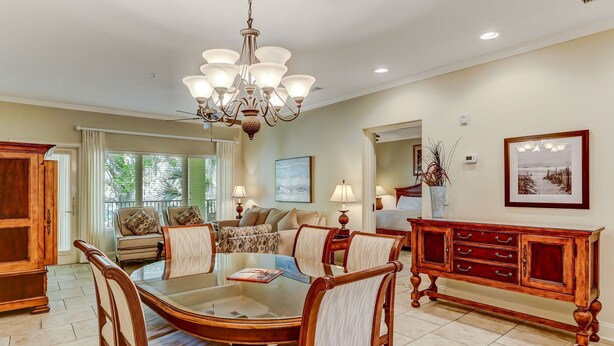 A dining area with a round table, chairs, a chandelier, and a wooden cabinet. - 2519-20 Tennis Villa-Charming 2 BR in Tranquil Setting on Amelia Island Omni! (Fernandina Beach)