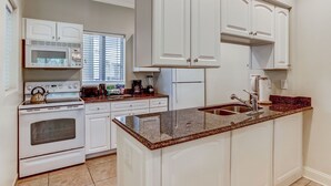 A kitchen with white cabinets, a granite countertop, a stove, and a sink. - 2519-20 Tennis Villa-Charming 2 BR in Tranquil Setting on Amelia Island Omni! (Fernandina Beach)