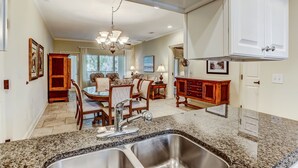 A kitchen with granite countertops, stainless steel sink, wooden cabinets, and a dining area with a chandelier. - 2519-20 Tennis Villa-Charming 2 BR in Tranquil Setting on Amelia Island Omni! (Fernandina Beach)