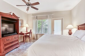 A hotel room with a bed, a desk, a television, and a ceiling fan.