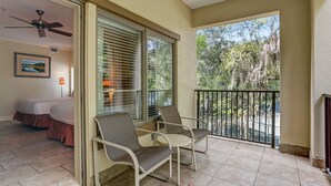 A balcony with two chairs, a ceiling fan, and a bed in the background. - 2519-20 Tennis Villa-Charming 2 BR in Tranquil Setting on Amelia Island Omni! (Fernandina Beach)