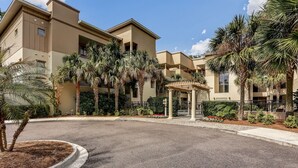 A multi-story hotel with a beige facade, palm trees, and a covered outdoor seating area.