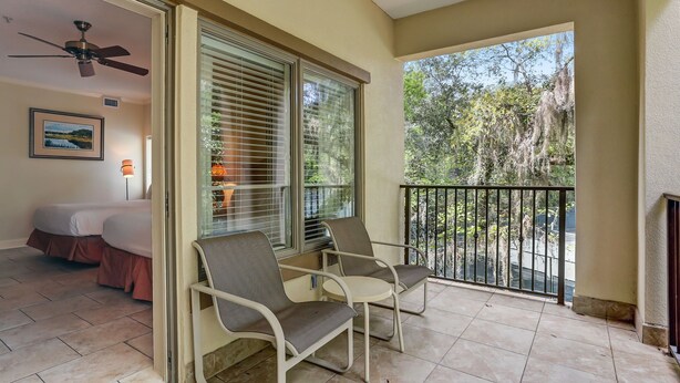 A balcony with two chairs, a ceiling fan, and a bed in the background.